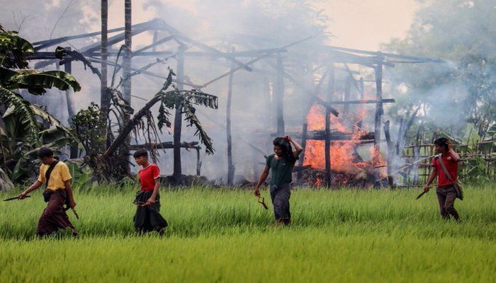 Unidentified men carry knives and slingshots as they walk past a burning house in Gawdu Tharya village near Maungdaw in Rakhine state, in northern Myanmar on September 7, 2017 AFP