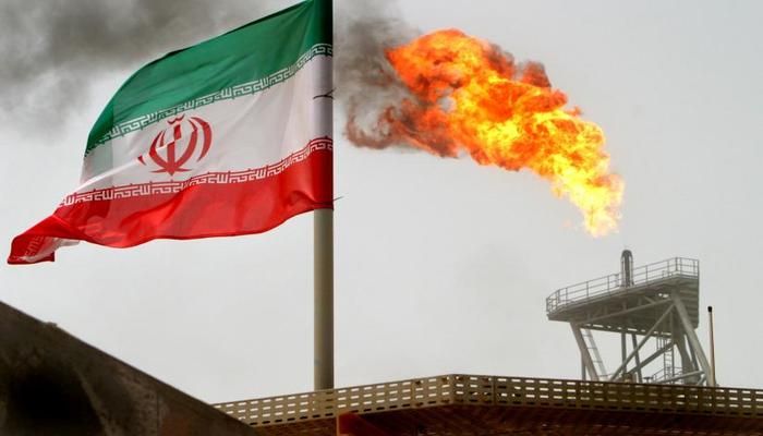 A gas flare on an oil production platform in the Soroush oil fields is seen alongside an Iranian flag in the Persian Gulf, Iran, July 25, 2005.  Photo: REUTERS