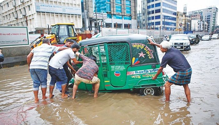 People trying to push a CNG-run three-wheeler out of a pothole on Kazi Nazrul Islam Avenue. Photo: Collected.
