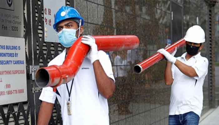 Construction workers wearing masks in precaution of the coronavirus outbreak carry pipes as they pass a building in the Central Business District in Singapore February 18, 2020 || Photo: Reuters 