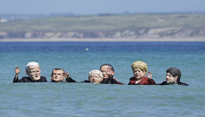 Protesters wearing giant heads portraying G7 leaders swim in the water during a demonstration outside the G7 meeting in St. Ives, Cornwall, England, on June 13, 2021 || Photo: AP
