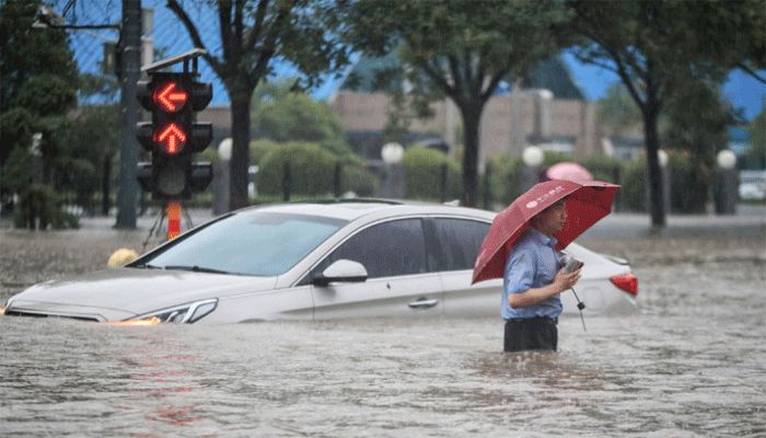 This photo taken on July 20, 2021 shows a man wading past a submerged car along a flooded street following heavy rains in Zhengzhou in China's central Henan province. || AFP Photo: Collected