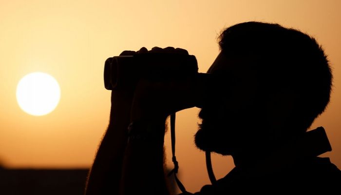 A crew member of the German NGO migrant rescue ship Sea-Watch 3 uses binoculars to keep watch for migrant boats at sunset in the search and rescue zone in international waters off the coast of Libya, in the western Mediterranean Sea, July 26, 2021. || REUTERS Photo: Collected