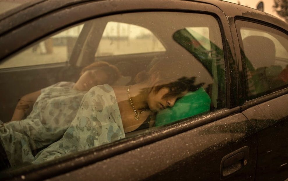 (Evia, Greece) A woman sleeps in her car on the beach as a wildfire rages in the village of Pefki on Evia island. A multinational force of nearly 900 firefighters were at the scene in a desperate effort to stop the conflagration enveloping the northern town of Istiaia. (Photograph: Angelos Tzortzinis/AFP/Getty Images)