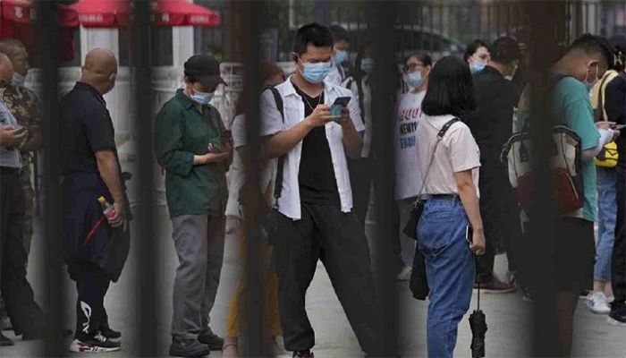 A man wearing a face mask to help curb the spread of the coronavirus browses his smartphone lining up with masked residents to receive their vaccine at a vaccination point at the Central Business District in Beijing, June 9, 2021. || AP Photo: Collected