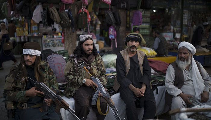 (Kabul, Afghanistan) Taliban fighters sit next to street vendors at a local market in Kabul || Photograph: Felipe Dana/AP