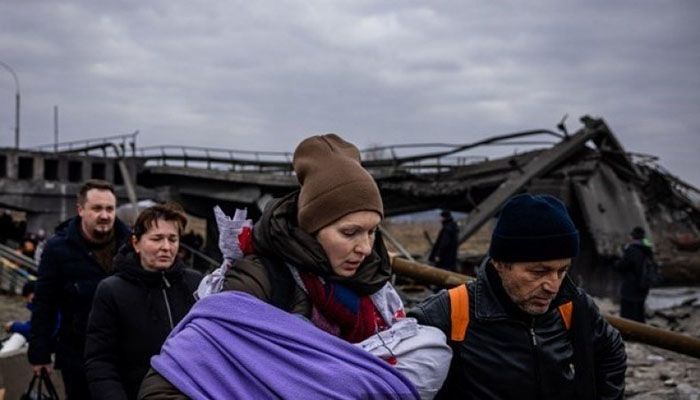 A woman carrying her baby crosses a destroyed bridge as they flee the city of Irpin, northwest of Kyiv, on March 7, 2022. || AFP Photo: Collected 