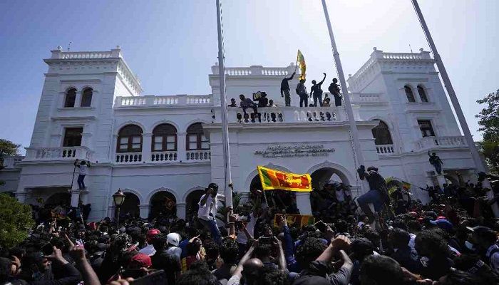 A protester, carrying national flag, stands with others on top of the building of Sri Lankan Prime Minister Ranil Wickremesinghe's office, demanding he resign after president Gotabaya Rajapaksa fled the country amid economic crisis in Colombo, Sri Lanka, Wednesday, July 13, 2022. 