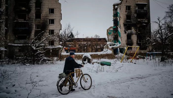 A resident pushes his bike on a snow covered street next to destroyed residential buildings in Borodyanka, near Kyiv on December 4, 2022, amid the Russian invasion of Ukraine. || AFP Photo