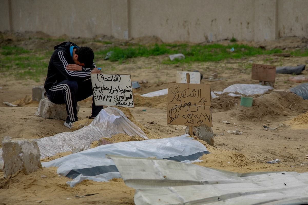 A young man sits by a shallow tomb at a makeshift cemetery in a residential neighbourhood near Gaza City's al-Shabiyah district || Photo: AFP