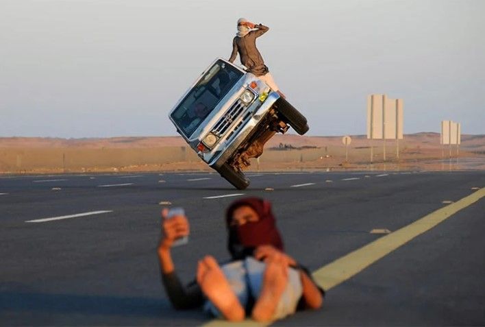 The photo of the driver of this car riding on two wheels while taking a selfie is a triumphant mix of risk and art. The photographer captures the scene as if the selfie taker is balancing the car with his head.