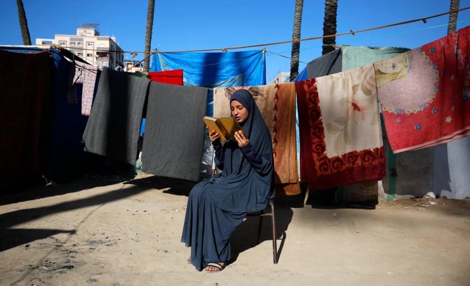 A displaced Palestinian woman reads the Quran during the last days of Ramadan, in a tent camp in Deir el-Balah.