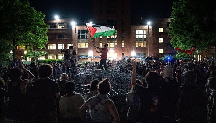 A man holds up a Palestinian flag as pro-Palestinian activists and students chant, surrounding piled barricades at an encampment at University Yard at George Washington University on April 29, 2024, in Washington, D.C || Photo: Kent Nishimura / Getty